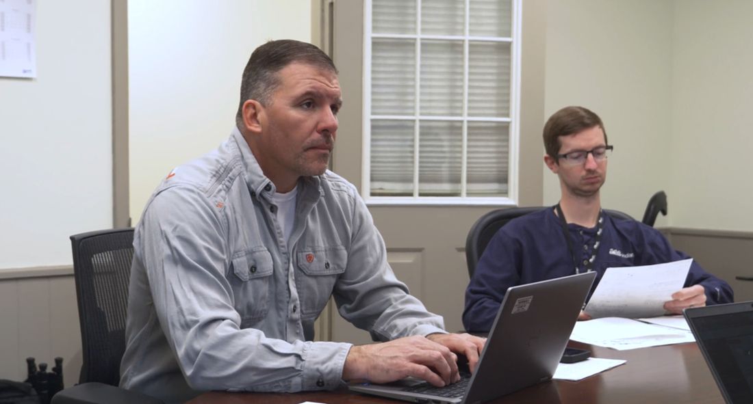 Two colleagues working side by side at a laptop in a meeting room