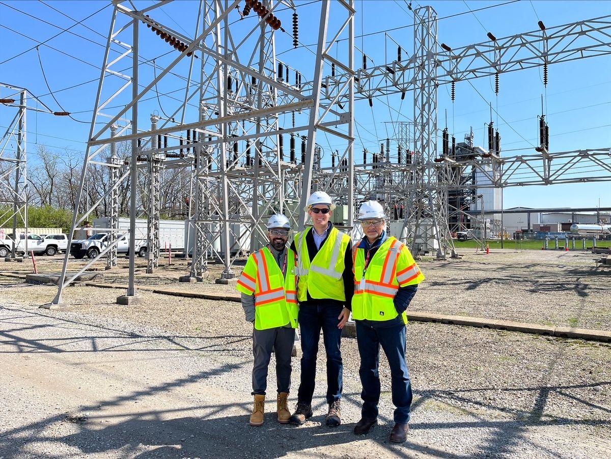 Three colleagues in hard hats and high-visibility vests standing together at an electrical substation