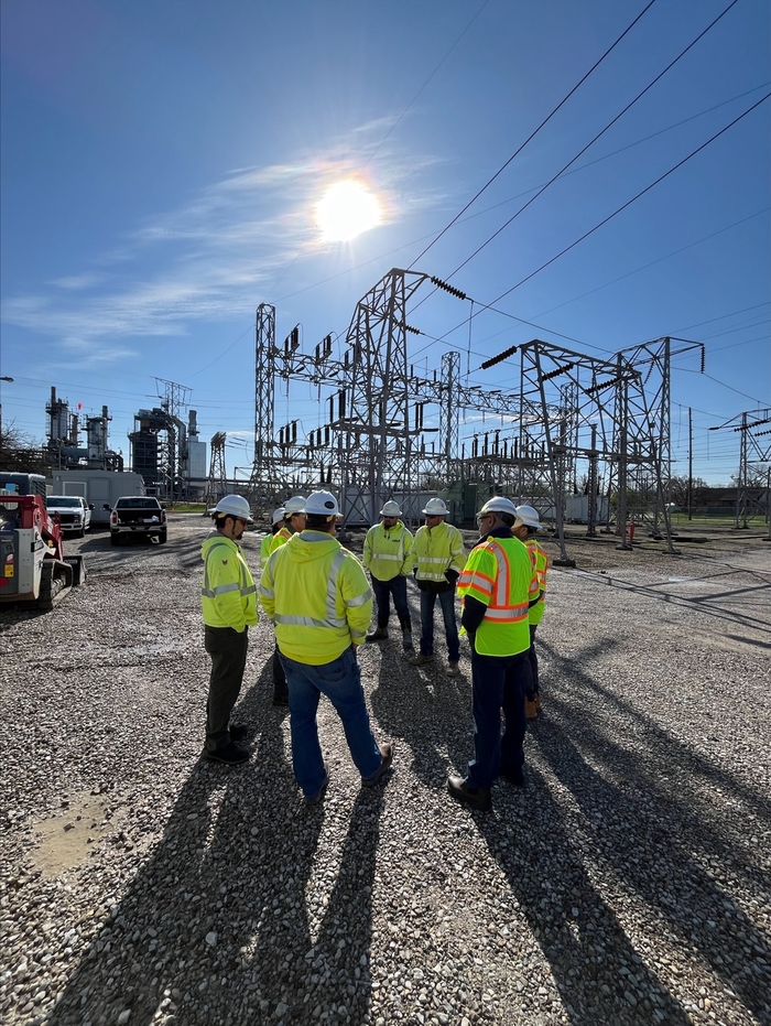 People in safety vests standing in a substation under power lines in the sun